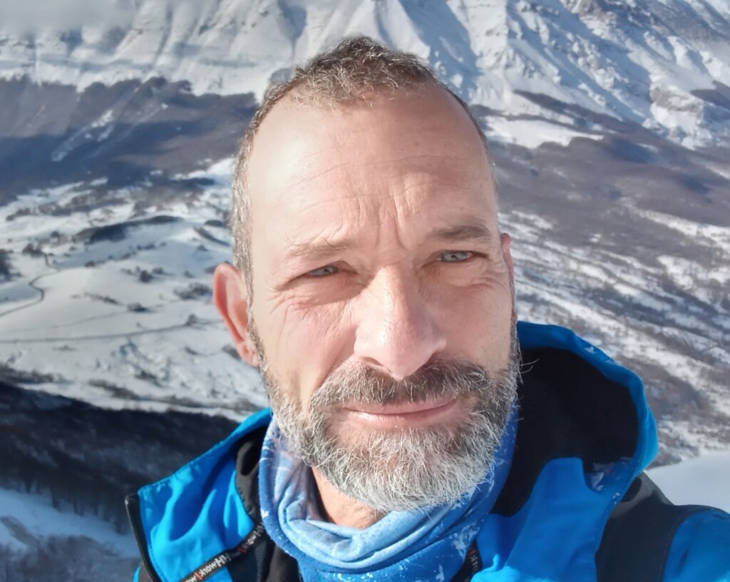 Carlo Meneghini, con una giacca dea neve blu e nera, sullo sfondo montagne innevate