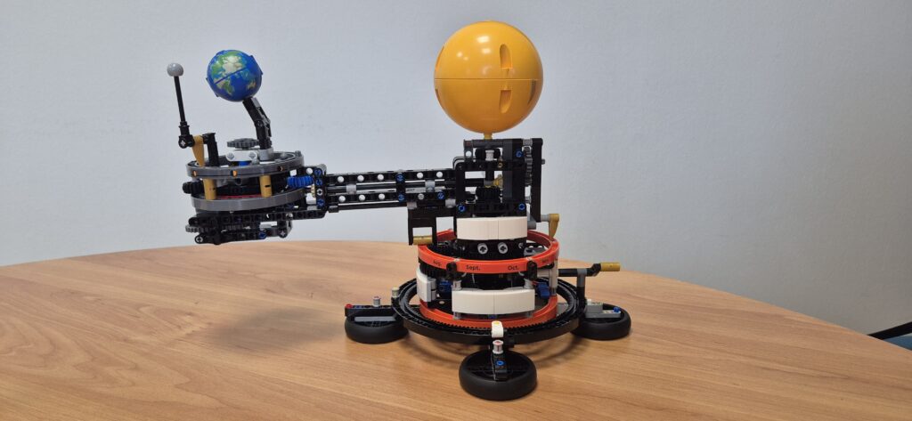 Il tellurio astronomico realizzato con il kit EGO® Technic. Ha un corpo centrale formato da più cilindri sovrapposti, in cima il Sole giallo, un braccio connesso al corpo centrale sostiene la Terra, più piccola, e la Luna, ancor più piccola. 